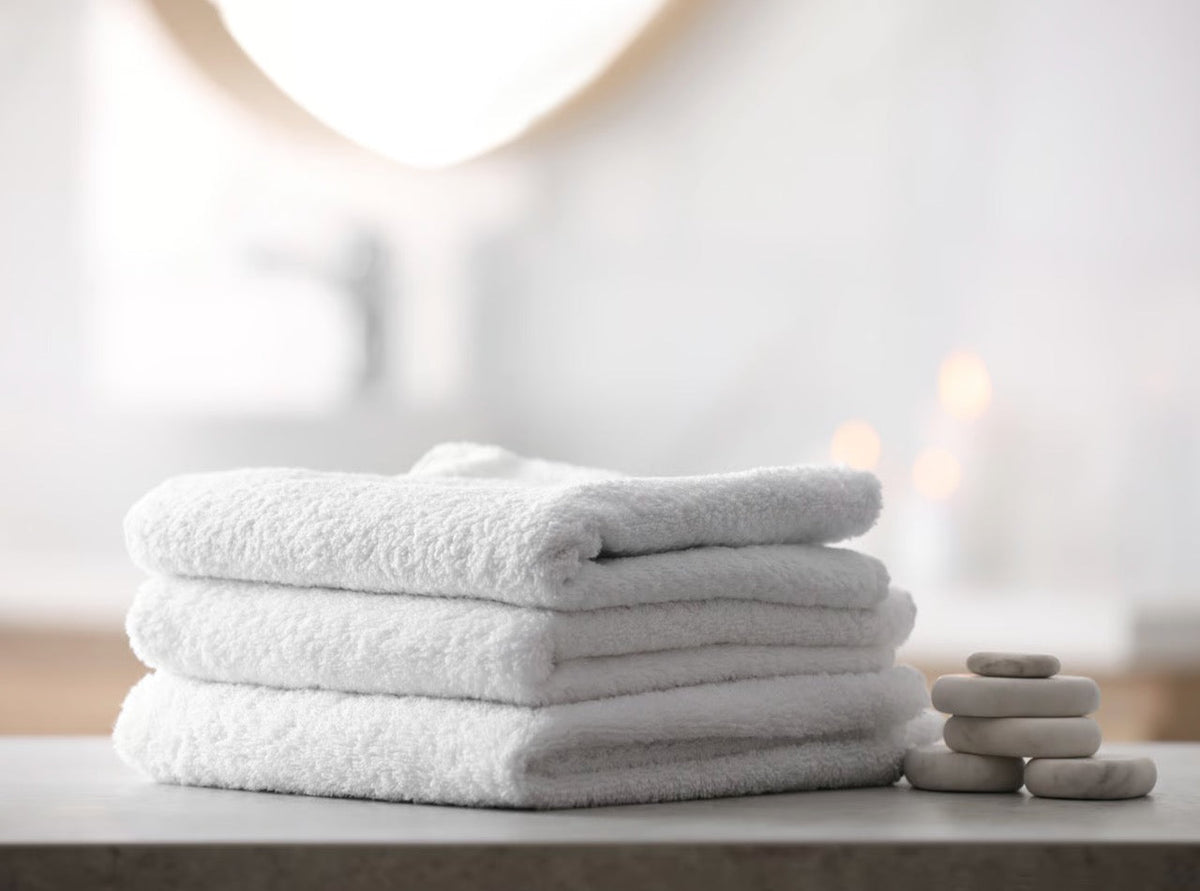 A stack of rolled white bath towels neatly arranged on a dark matte slate shelf in an upmarket hotel bathroom