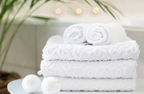 A neatly folded stack of thick white cotton towels resting on a white tray beside a lush green plant
