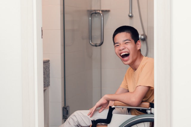 A laughing young man in a modern bathroom, symbolising the dignity and peace of mind found in independent living.